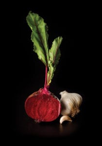 A bright red beet and a full garlic clove against a black background.