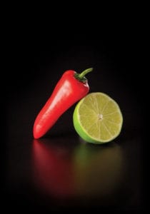A fresh red pepper and a lime rest on a black background.