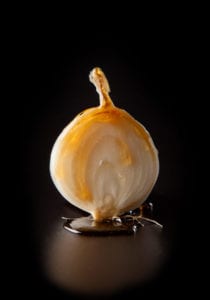 An onion and maple syrup resting together on a black background.